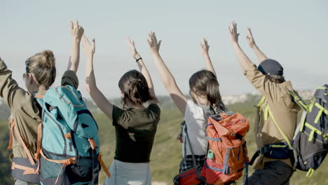 back view of family standing on cliff edge, raising their arms and enjoying the view