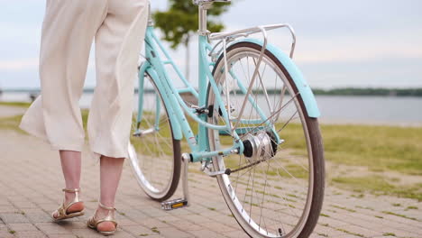 young woman walking a bike in slow motion beside a lake