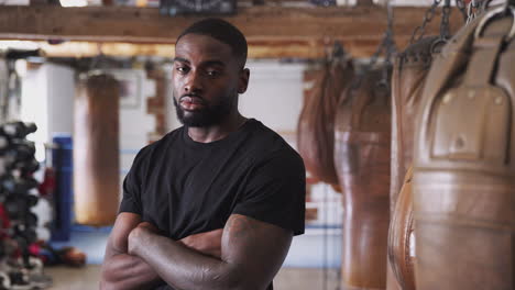 Portrait-Of-Male-Boxer-In-Gym-Standing-By-Old-Fashioned-Leather-Punch-Bag