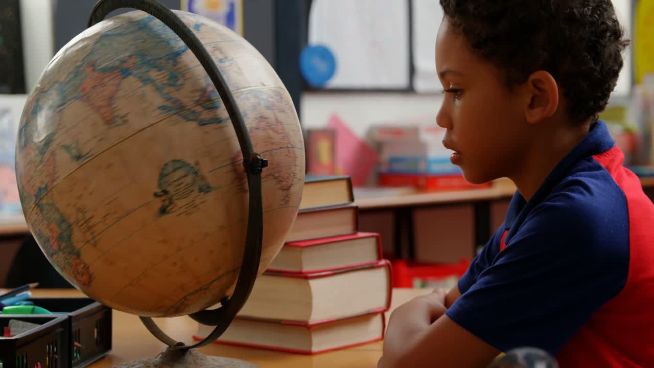 vista lateral de un escolar afroamericano estudiando el globo en el escritorio en el aula de la escuela 4k