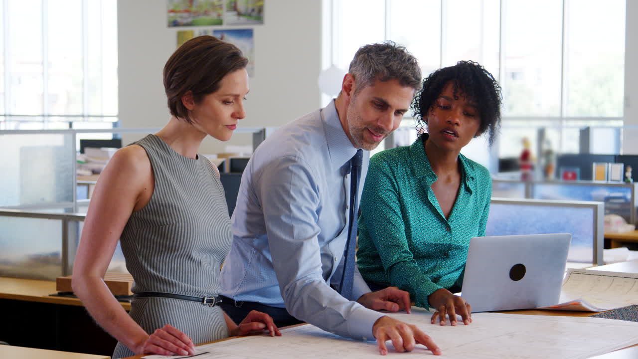 tres arquitectos discuten planes de diseño en una oficina