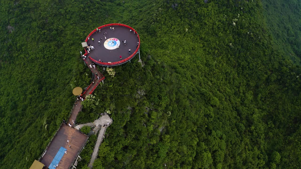 Una vista discendente mostra una piattaforma circolare rossa in cima a lussureggianti scogliere carsiche a Yangshuo Gulin. Pendii verdi circondano la struttura fondendo natura e design per filmati di viaggio suggestivi