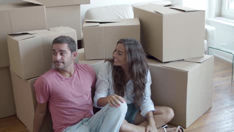 young caucasian couple sitting on floor near carton boxes and discussing interior