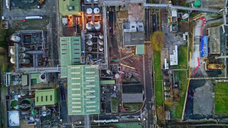 Overhead-aerial-footage-of-a-large-industrial-plant-showing-pipework-structures,-industrial-buildings,-cooling-towers,-steam,-and-work-vehicles