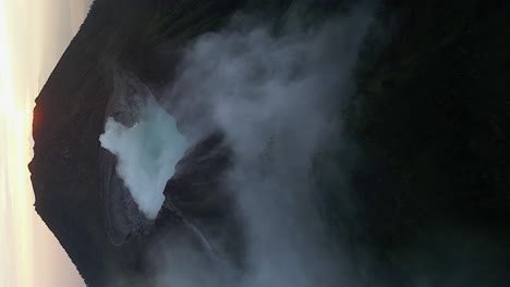 vertical format: morning sun behind volcano cone and smoking crater