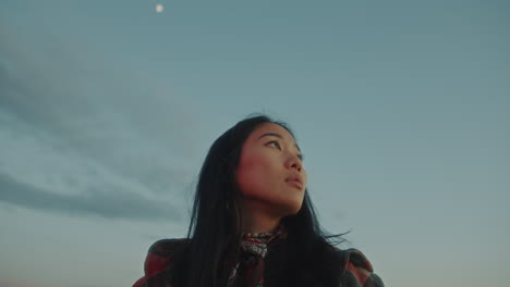 young asian woman standing in nature, looking up at evening sky