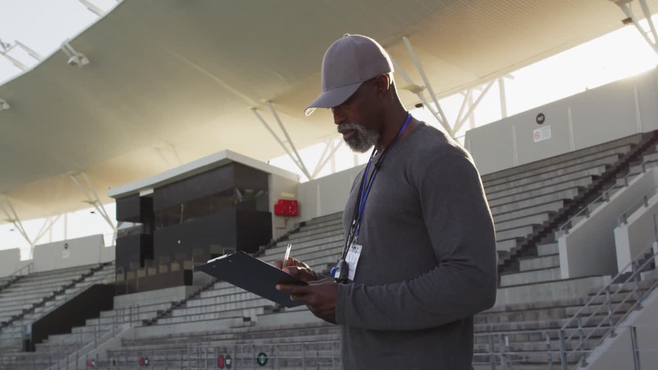 Smiling african american male coach making notes on sunny day