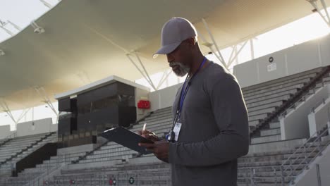 un entrenador afroamericano sonriente haciendo notas en un día soleado