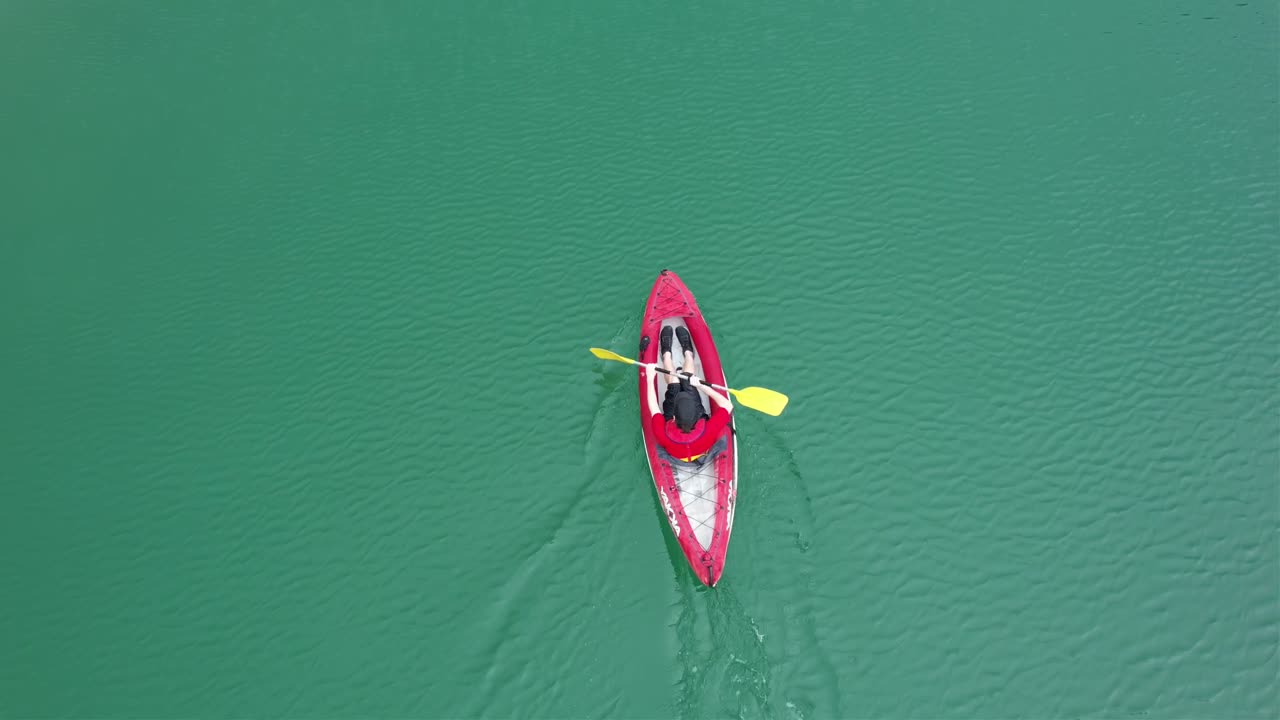 Boy wearing a red shirt and a cap rowing in his kayak over green waters