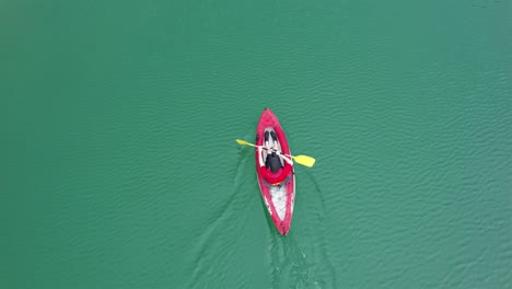 boy wearing a red shirt and a cap rowing in his kayak over green waters