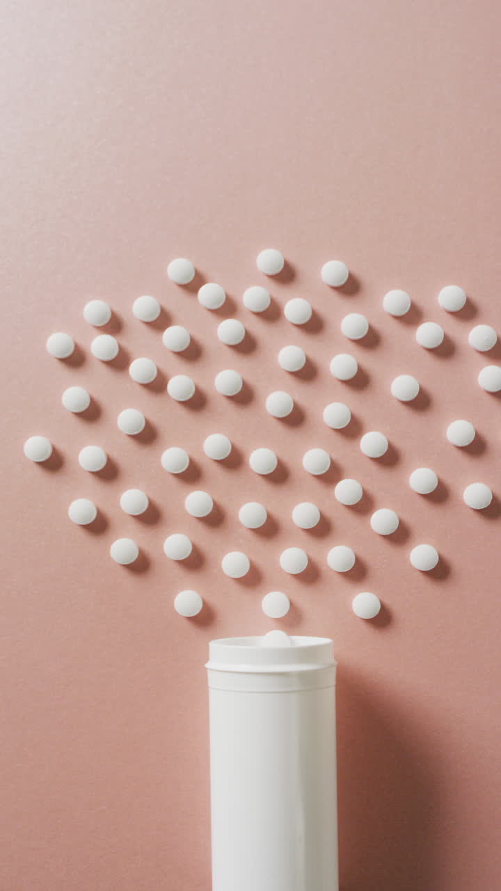 복사 공간과 함께 분홍색 배경에 열린 알약 상자와 색 알약의 수직 비디오