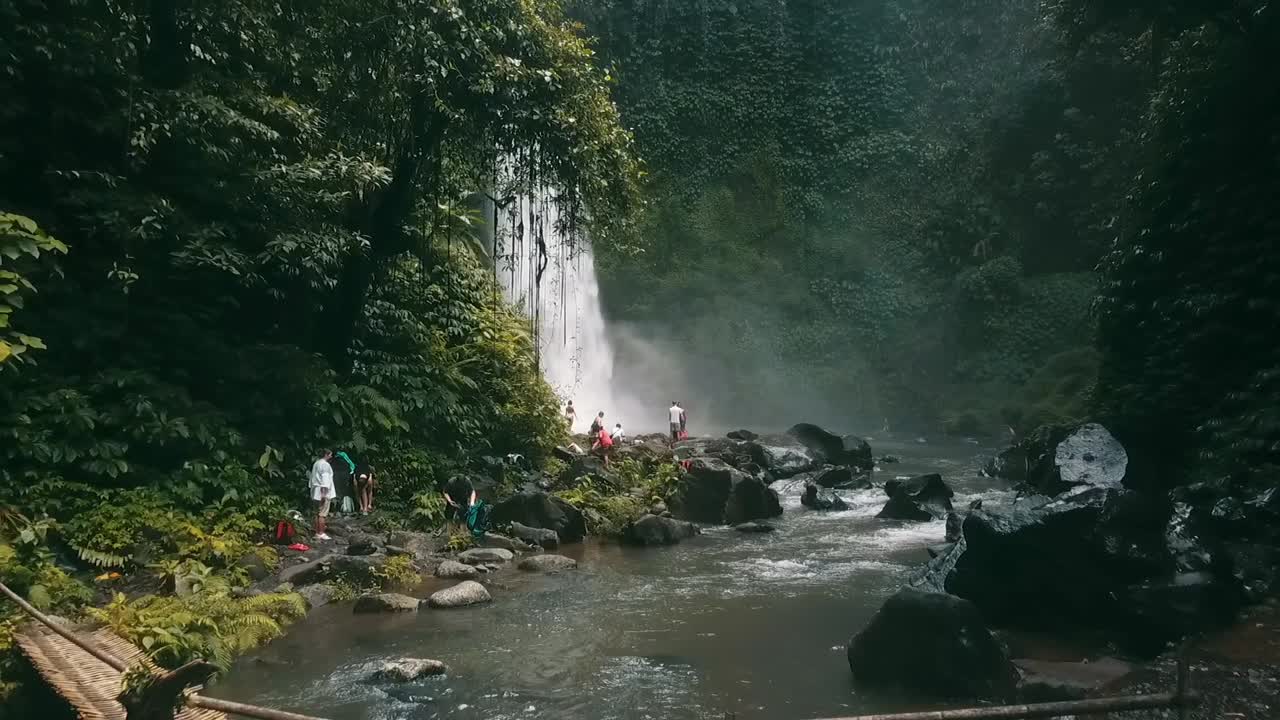 bali, primavera de 2020 en 1080 60p, durante el día, vuelo cinemático de drones largo vuelo lento hacia atrás desde una cascada sobre el río hasta un puente indígena