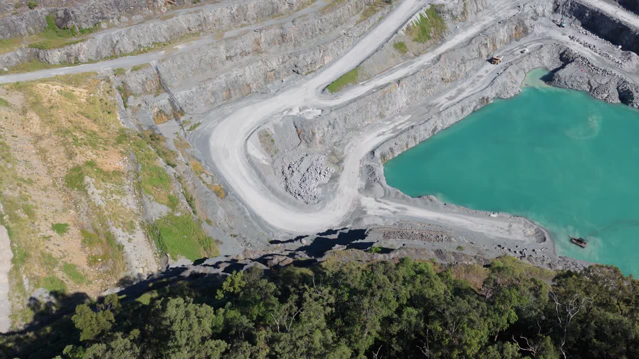 Aerial footage of a quarry with vibrant turquoise water, surrounded by lush greenery under bright daylight
