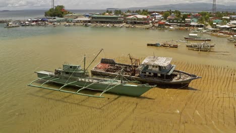 aerial dolly shot over shipwrecked fishing vessels beached in shallow waters off a coastal fishing village in surigao, philippines