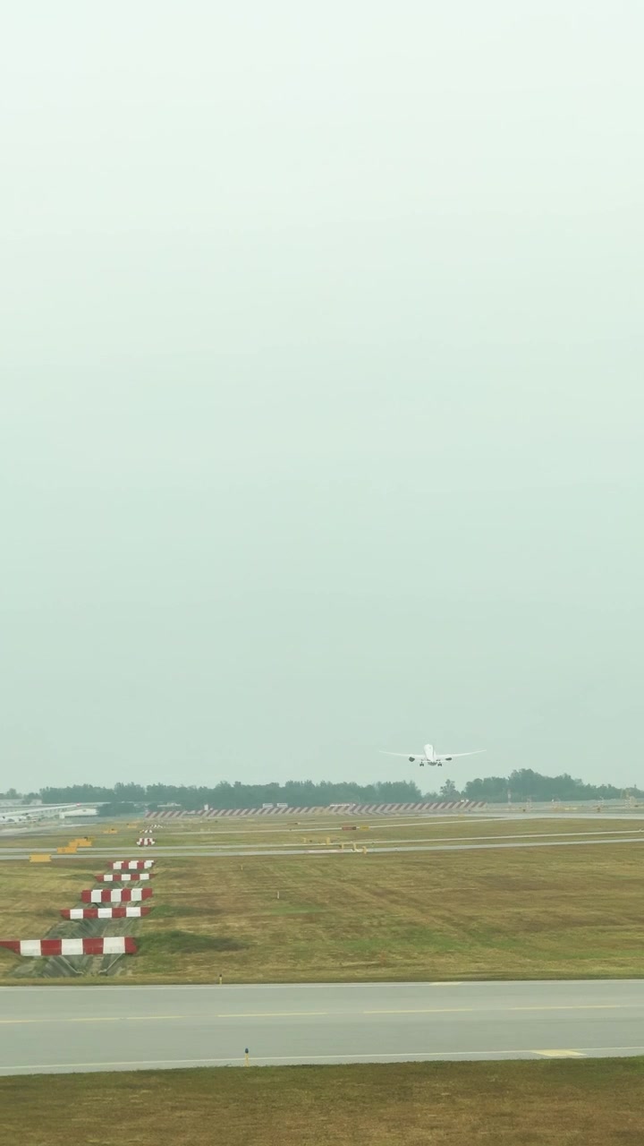 Ein entferntes Passagierflugzeug sinkt unter bedecktem Himmel in Singapur auf eine Landebahn zu.