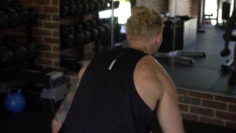 tattoo man muscles in home gym doing seated lateral shoulder raises shot from behind