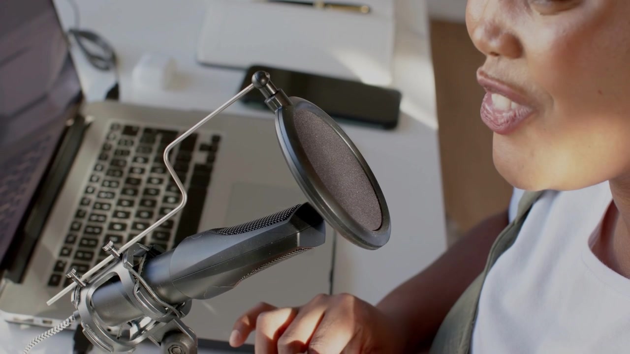 Donna conduttrice che si sporge in avanti parlando al microfono, registrando un podcast con onde che appaiono sopra il laptop