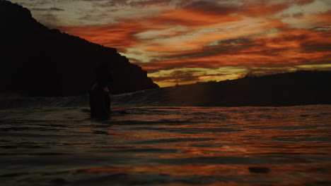 Pan-across-fire-red-sunset-sky-with-ocean-wave-breaking-and-mist-spreading-as-photographer-takes-final-breath-to-dive-below