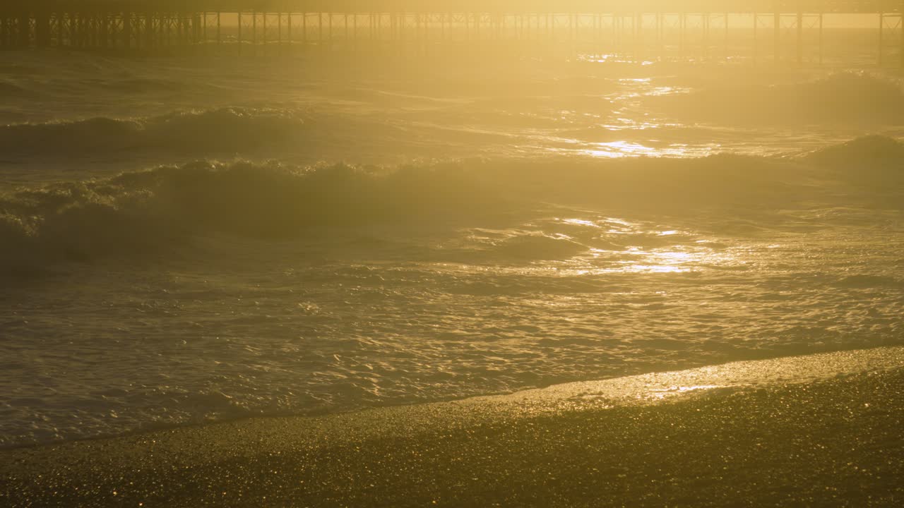 Rich Sunset Lighting as Waves Crash onto Brighton Beach as Sun Shines Remaining Light onto Pebble Beach. Slow Motion Nature Clip