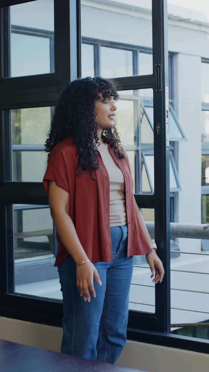 Vertical video: African American woman gazing at metal window, reaching handle, crossing arms