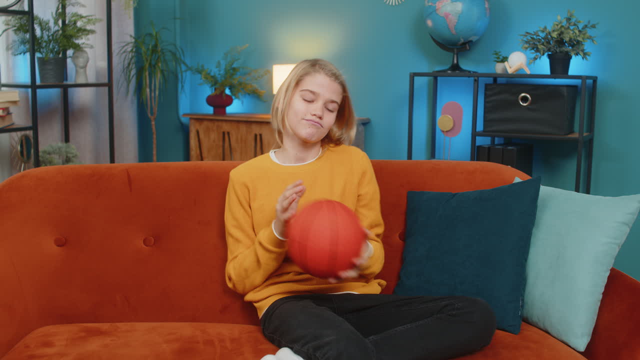 Teenager boy on home sofa actively enjoying playing with basketball bouncing ball trying to catch it