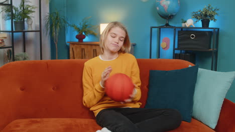 teenager boy on home sofa actively enjoying playing with basketball bouncing ball trying to catch it