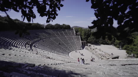 tourists visiting the famous ancient theatre of epidaurus on the west side of cynortion mountain on a sunny day in greece. - pan down