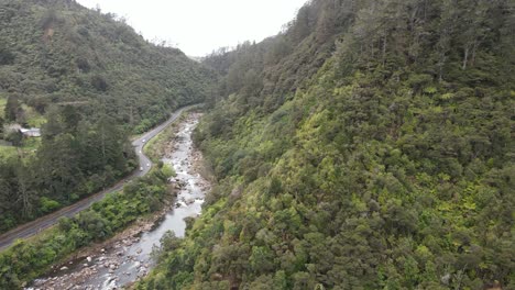 Video-Aéreo-De-Una-Carretera-Panorámica-Que-Serpentea-Por-El-Corazón-De-Un-Valle-Exuberante,-Junto-A-Un-Río.