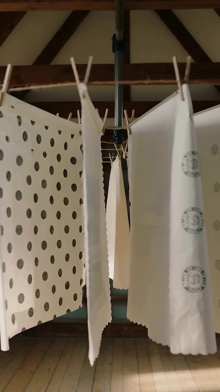 Vertical video: Rotating airer revealing polka-dot and crest-print towels in loft with clips