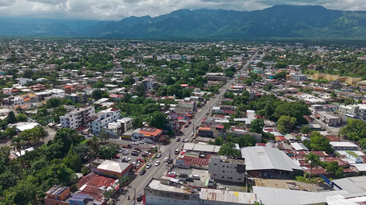 Bonao cityscape, city streets, buildings, residential areas, and mountain landscape in background, Dominican Republic. Aerial forward