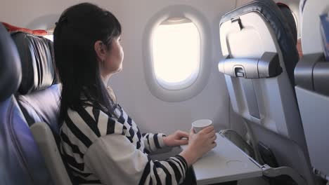 woman sitting inside airplane and looking at window and drinks coffee.