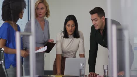 Diverse-group-of-business-colleagues-in-discussion-in-meeting-room-using-laptop-and-tablet-smiling