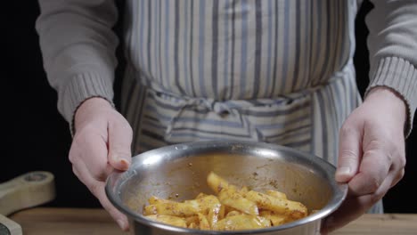 a hobby chef tosses raw potato wedges in a metal bowl to distribute the spices