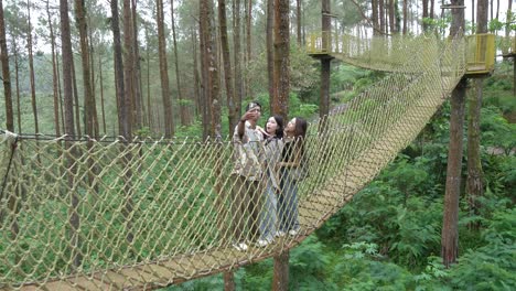 asian friends taking selfie on forest rope bridge in indonesia