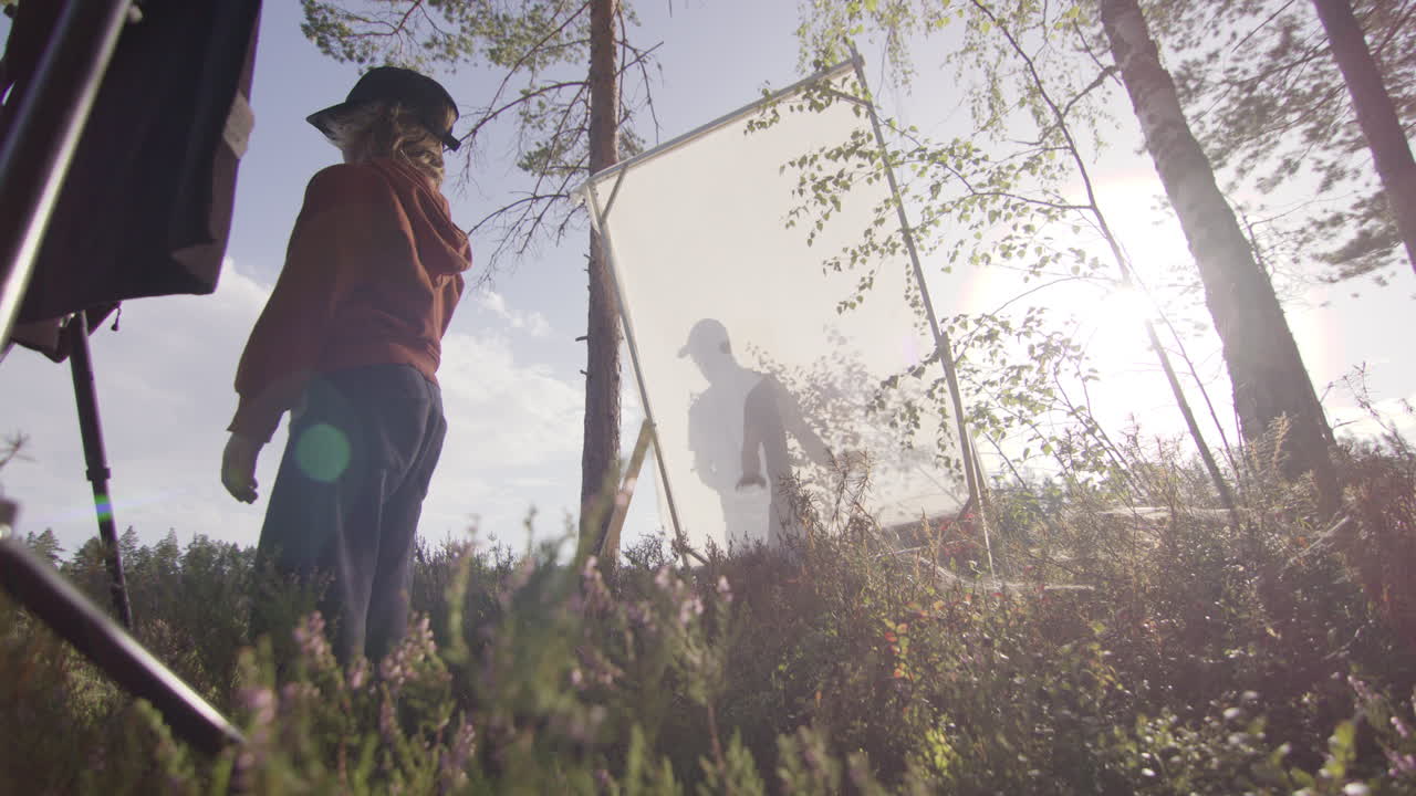 Videographer softens direct sunlight on subject using diffusion sheet in woods