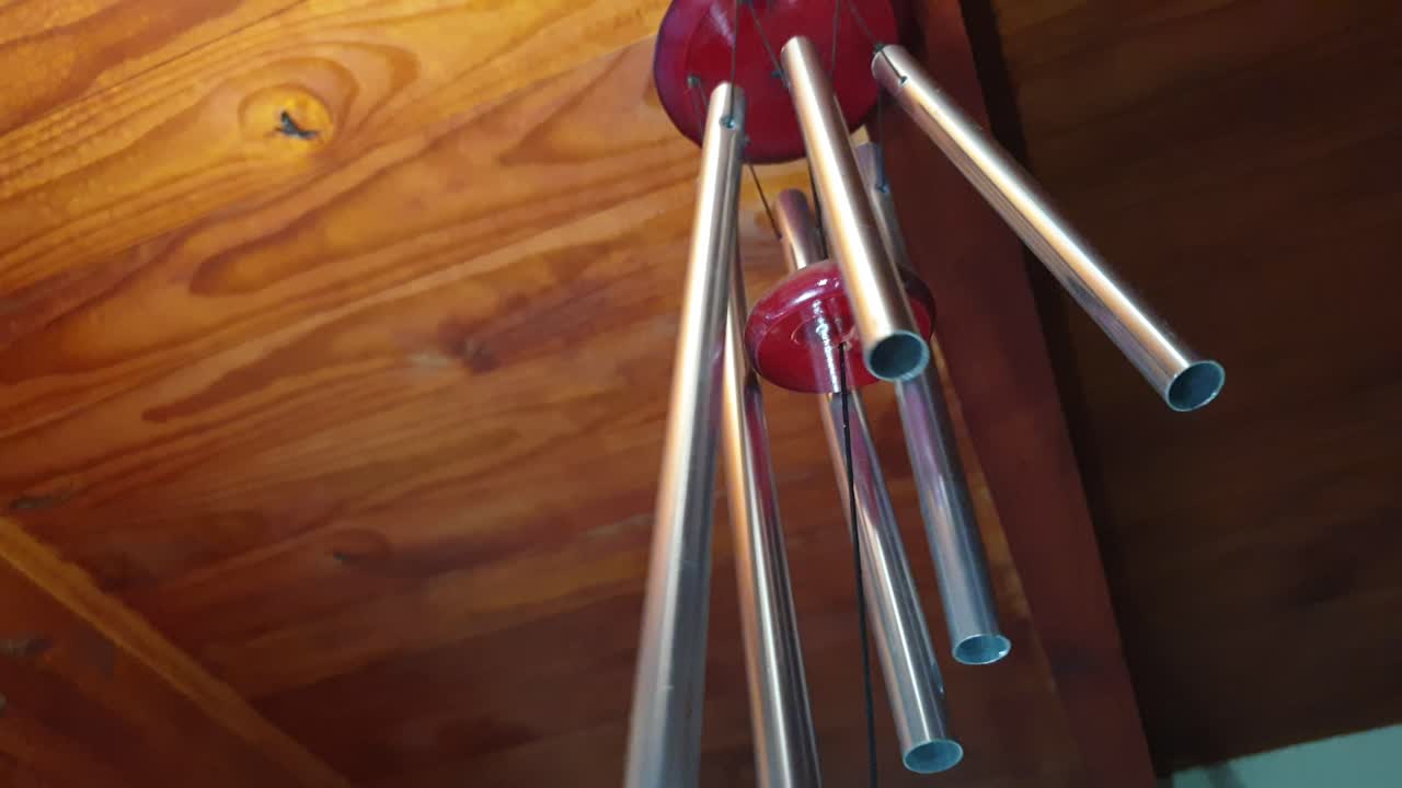 campanilla de viento de tubo de metal de aluminio que se mueve y golpea entre sí mientras el viento los mueve y hace que la música suene debajo del techo de madera