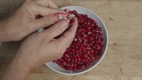 Top-down,-wide-shot-of-pomegranate-being-peeled-in-to-a-white-ceramic-bowl