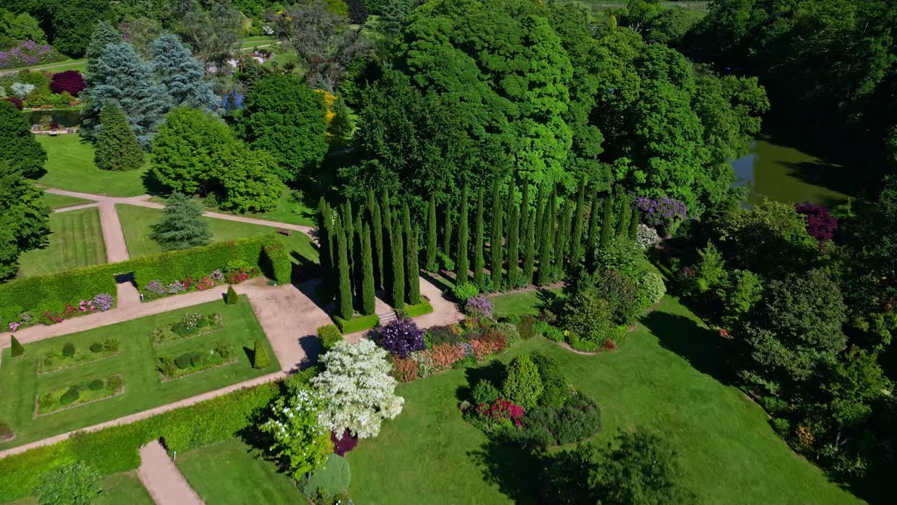 Drone moves backward revealing trimmed trees, plants, paths, and greenery in Haute Bretagne Botanical Garden on a sunny day - France