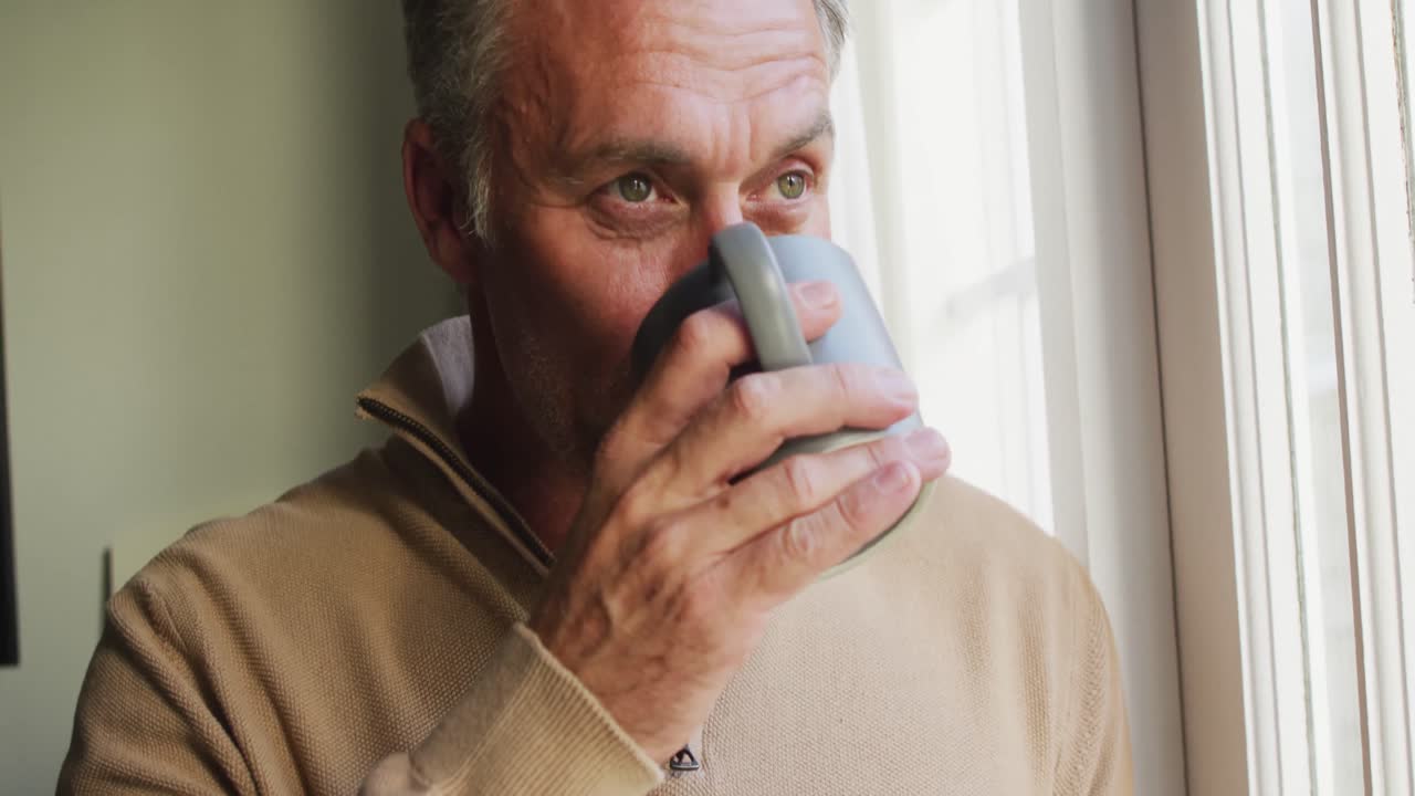 Uomo caucasico felice che guarda fuori dalla finestra e beve caffè in camera da letto