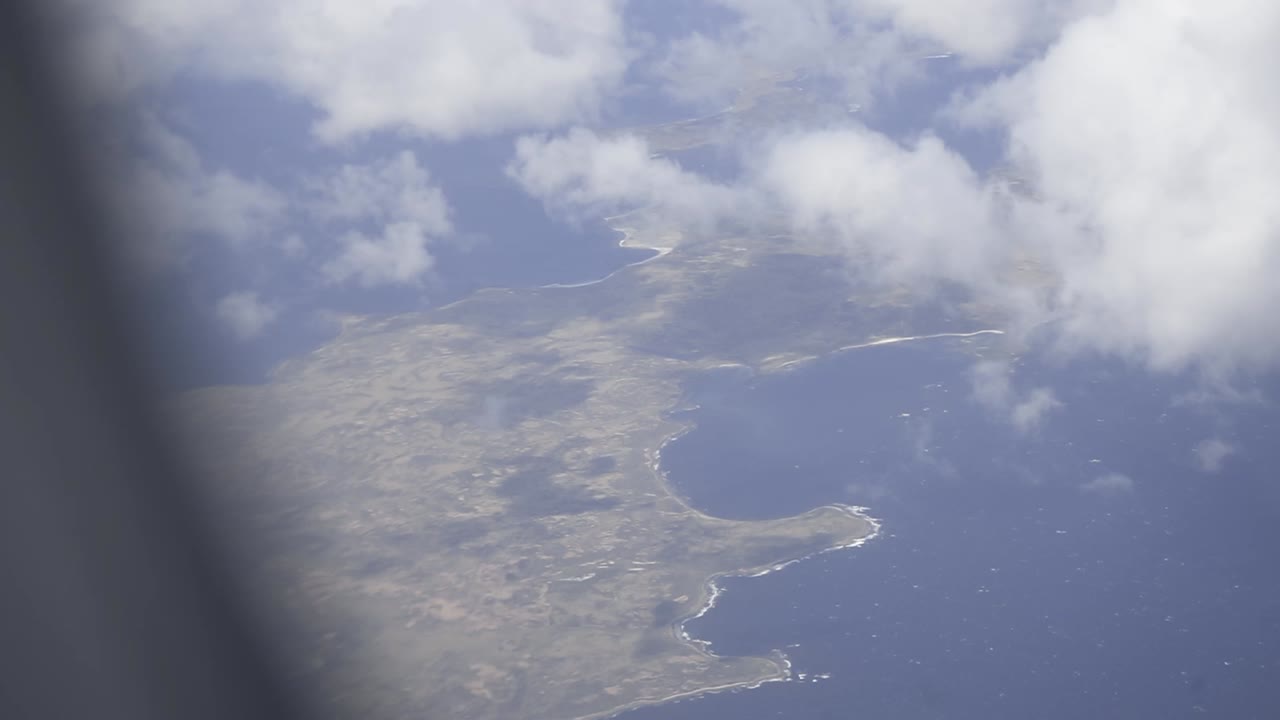 Aerial panorama revealing lanzarote's dramatic volcanic coastline, white clouds drifting over rugged rocky terrain and azure atlantic waters