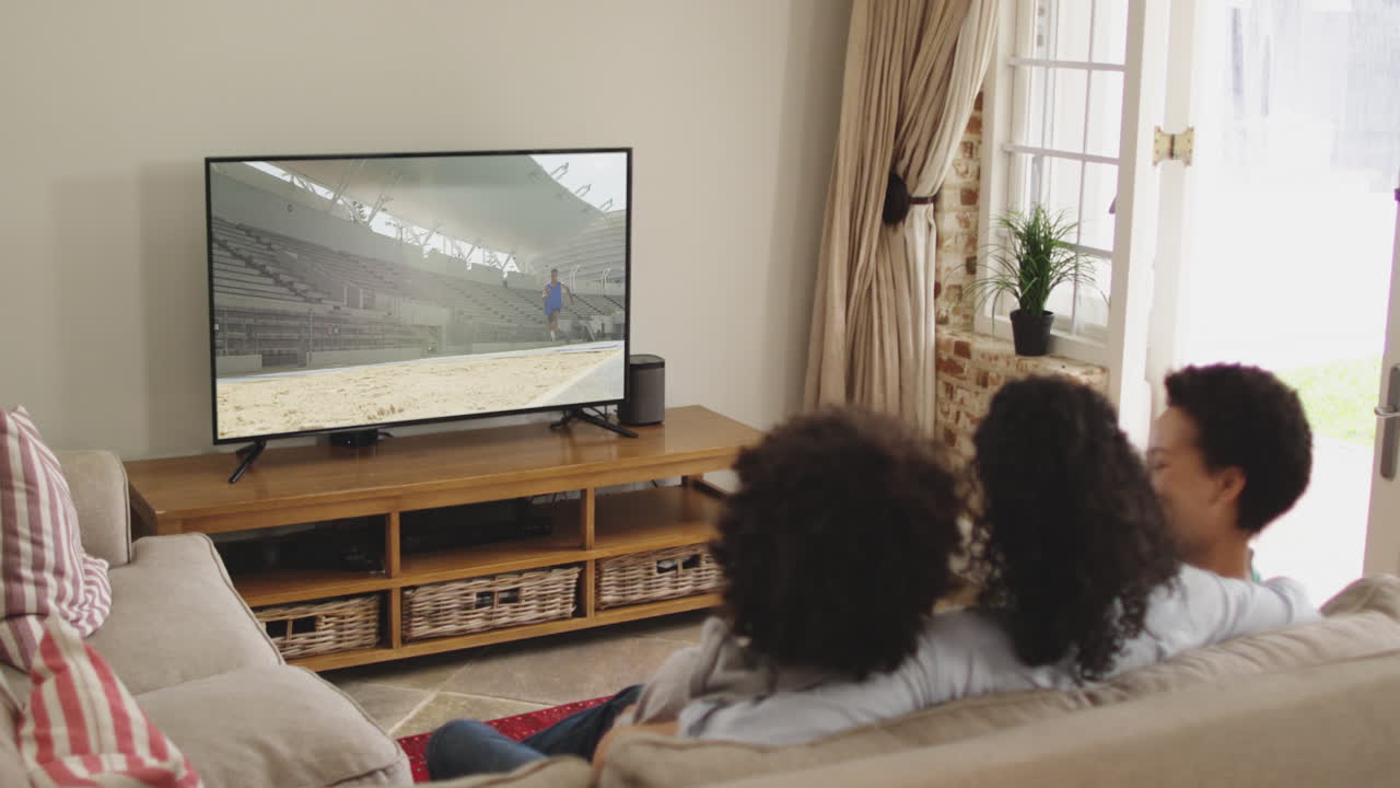 Composizione: famiglia felice seduta a casa insieme che guarda l'atletica del salto in lungo in TV.