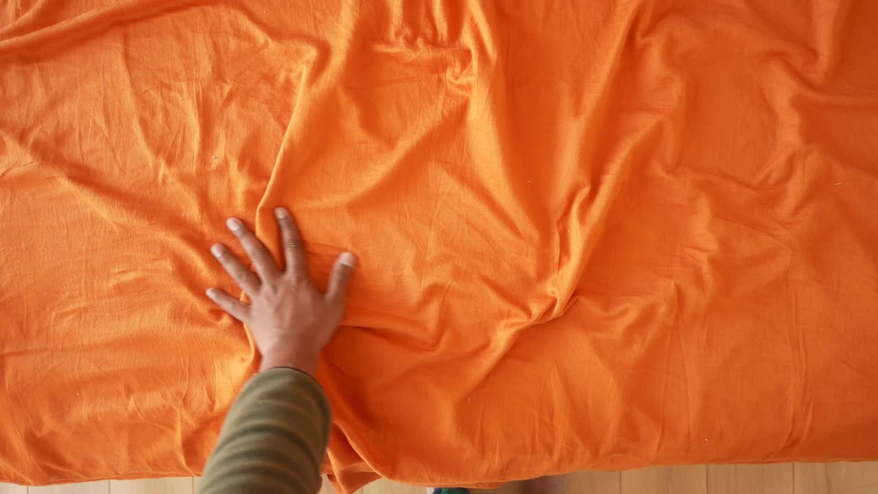 Hand einer Person auf einem orangefarbenen Bettlaken