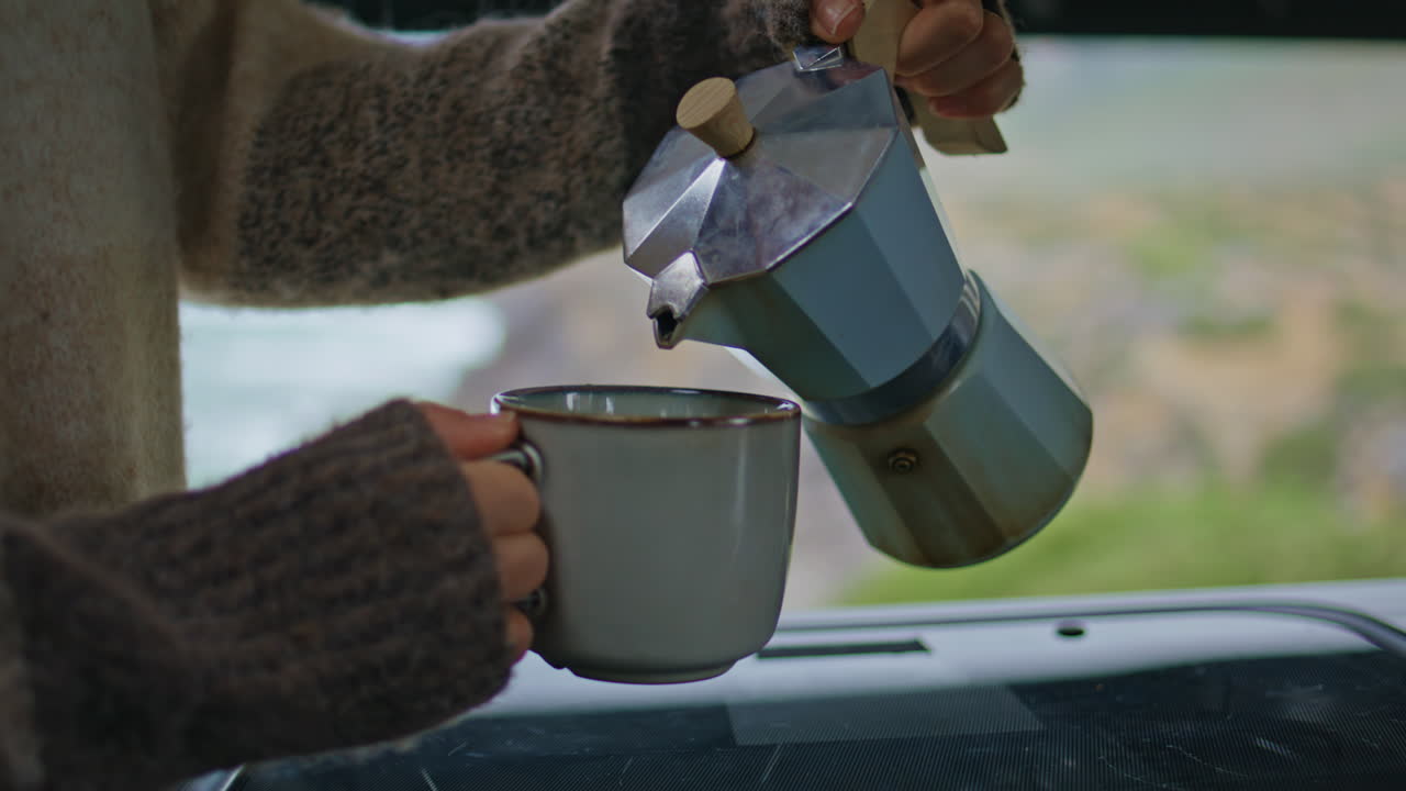 Mani di donna che versano l'espresso nella tazza godendosi la mattinata nel camper, primo piano.