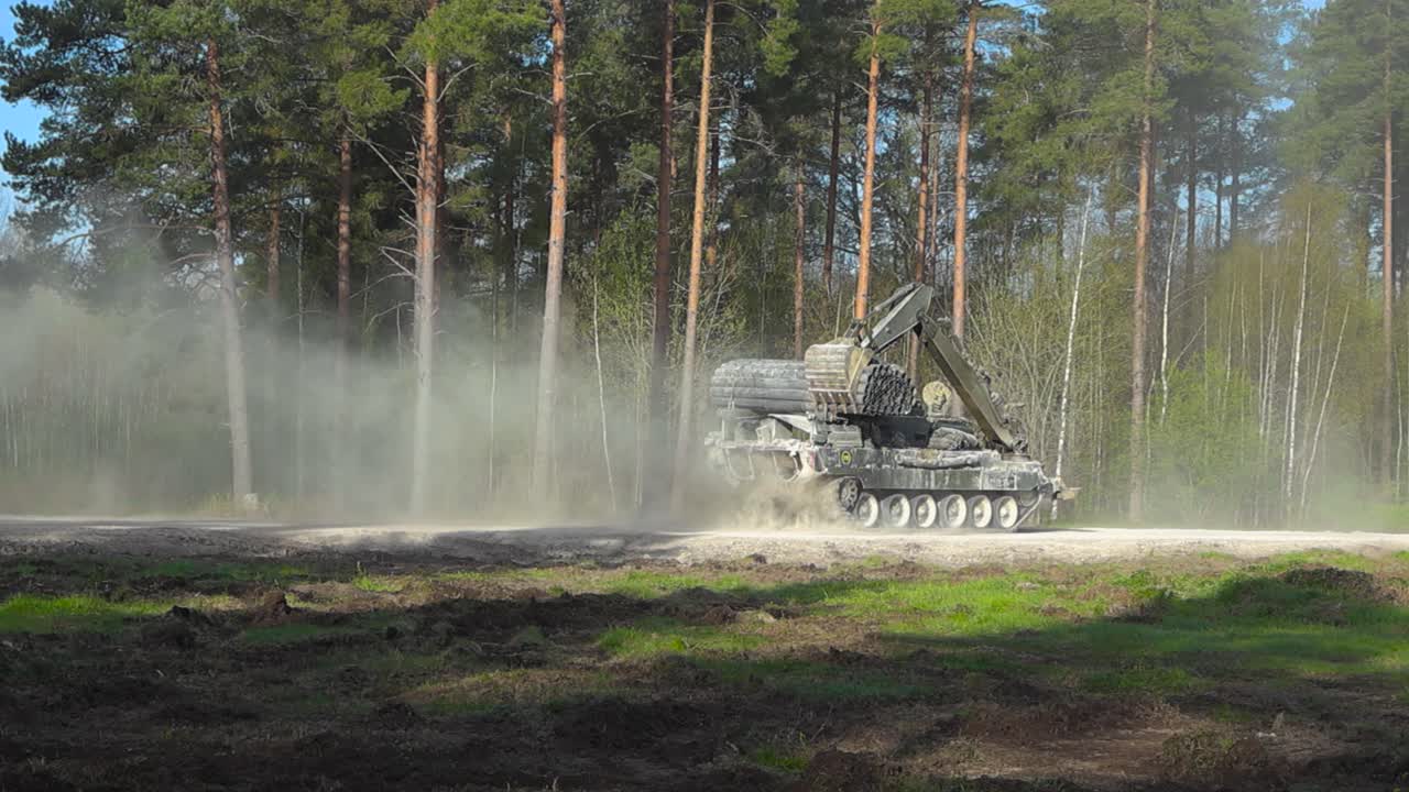 British Challenger 2 combat engineering vehicle tank with excavator arm and mine plough speeding on a gravel forest countryside road with a dust cloud behind it during a sunny summer day, into war.