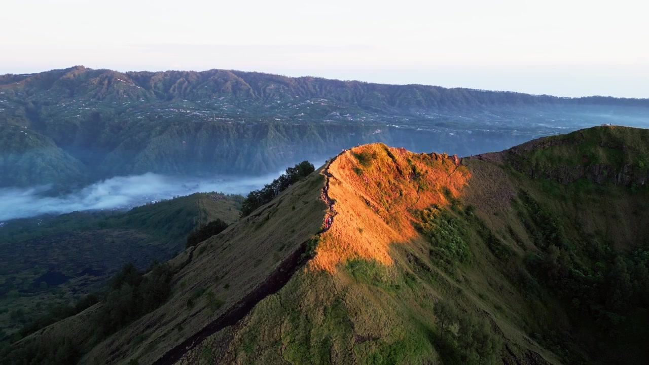 Avventurieri in escursione lungo un'aspra cresta montuosa con la luce brillante dell'alba, atmosfera nebbiosa della valle e un aspro paesaggio vulcanico. Filmato aereo con drone in allontanamento