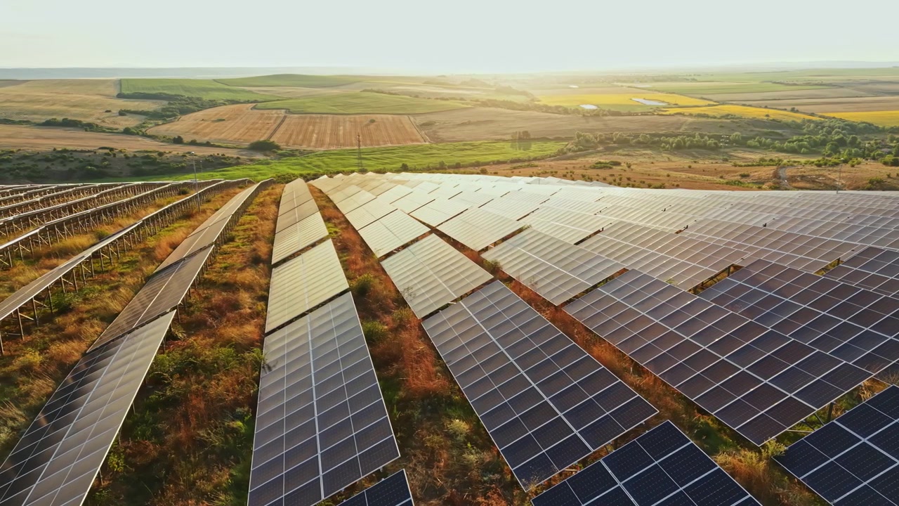 Solpaneler installeret på en skråning under solnedgang i et landområde, der fremviser teknologi for vedvarende energi