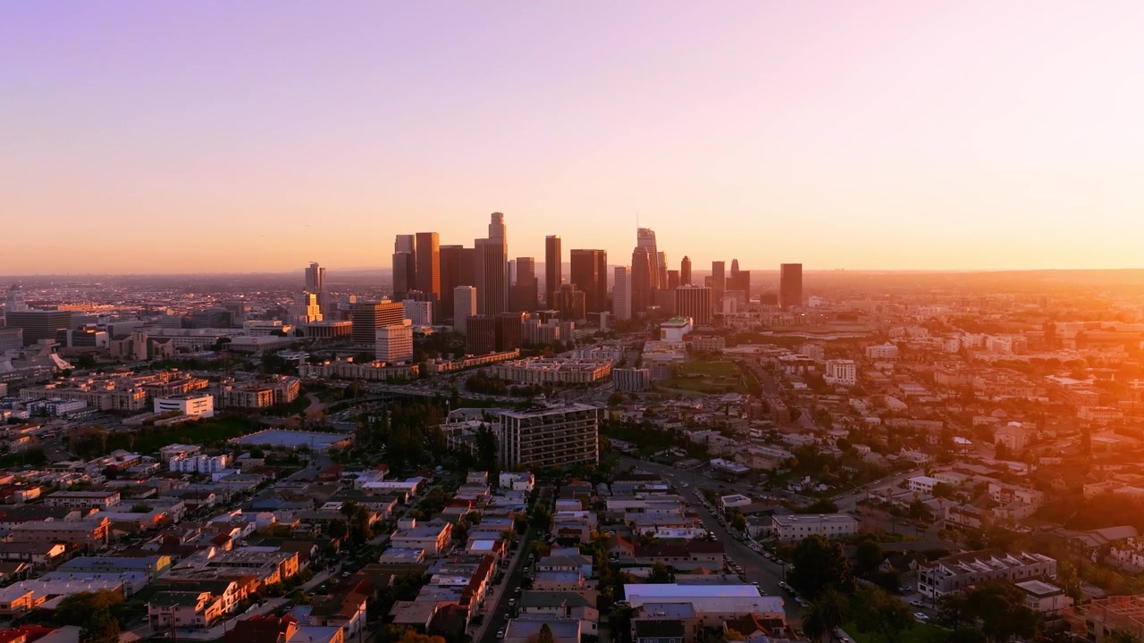 La vista aerea cattura lo skyline del centro di Los Angeles al tramonto. Il traffico pendolare scorre per le strade urbane. L'infrastruttura cittadina mostra lo sviluppo nell'area metropolitana.