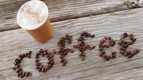 disposable cup and coffee written with coffee beans