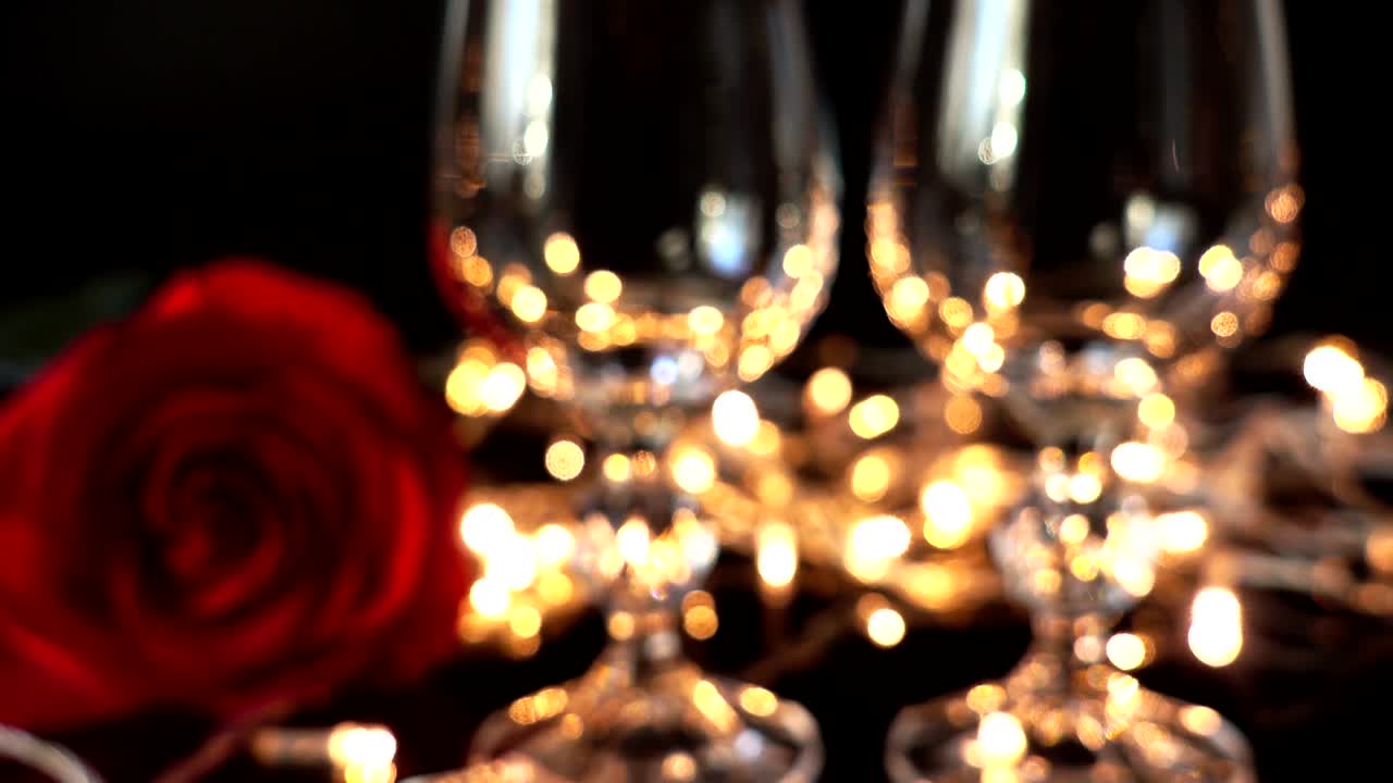 Copas de vino y rosa sobre el fondo de guirnaldas brillantes. Desenfoque