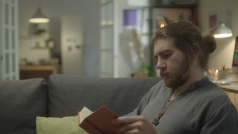 man reading book in evening at home